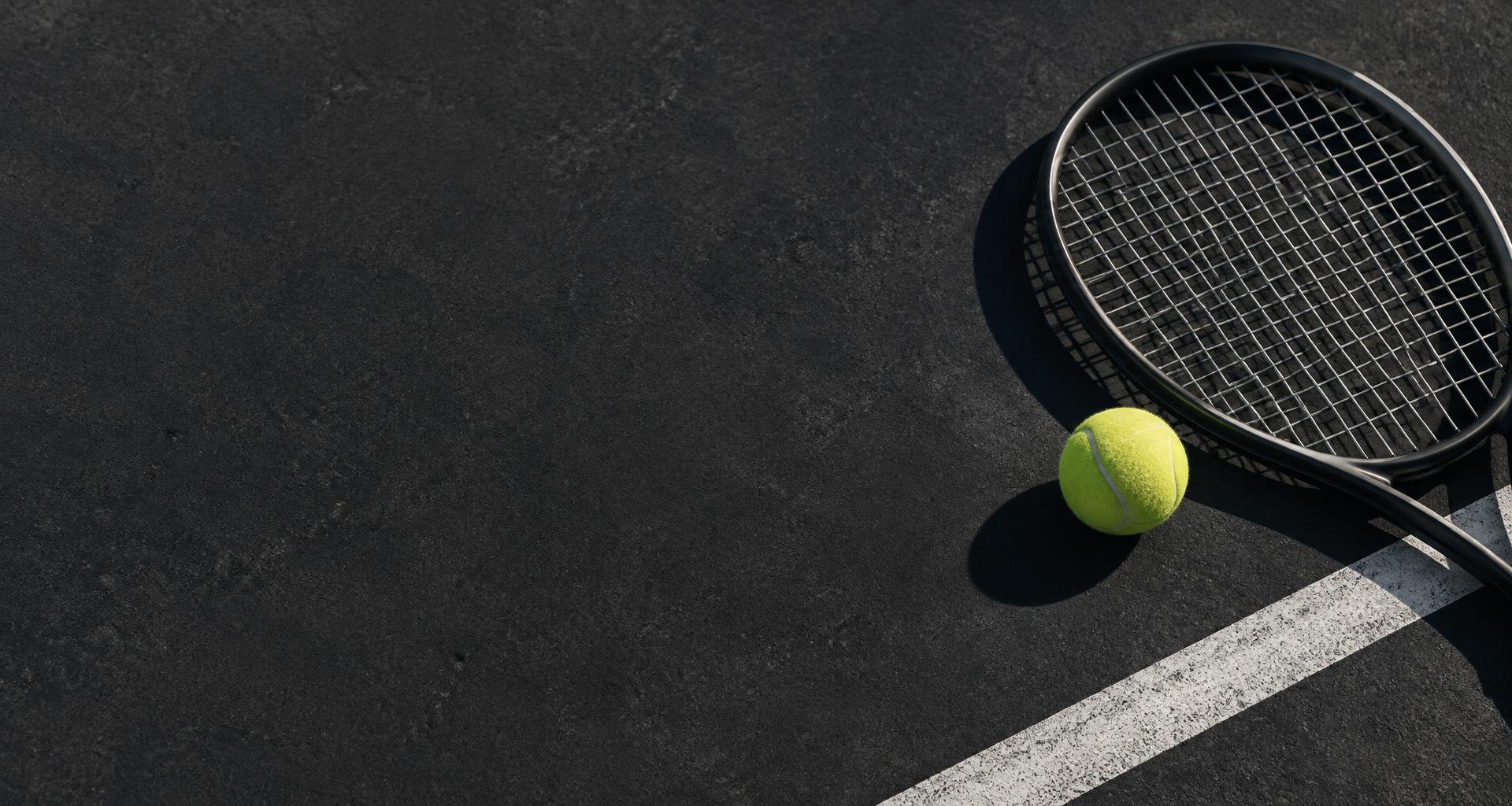 A graphite racquet and tennis ball on a charcoal court surface